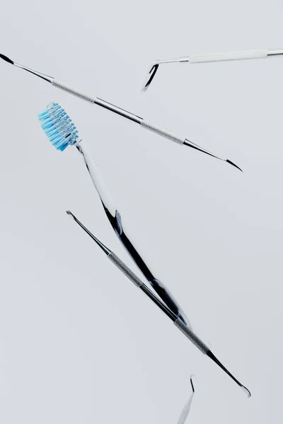Instrumentos de metal dental y cepillo de dientes con cerdas azules aisladas sobre fondo gris - foto de stock