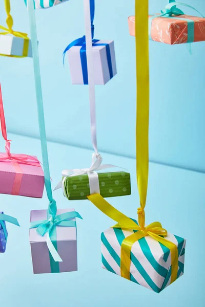 Festive colorful gift boxes hanging on ribbons on blue background — Stock Photo