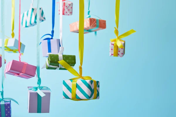 Festive colorful gift boxes hanging on ribbons on blue background — Stock Photo