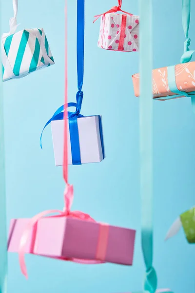 Selective focus of festive colorful gift boxes hanging on ribbons isolated on blue — Stock Photo