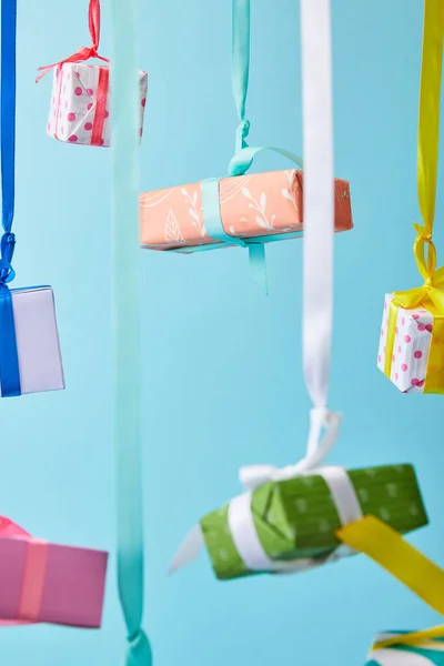 Enfoque selectivo de las cajas de regalo de colores festivos colgando de cintas aisladas en azul - foto de stock