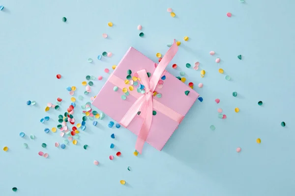 Vista superior de confeti colorido cerca de caja de regalo rosa sobre fondo azul - foto de stock