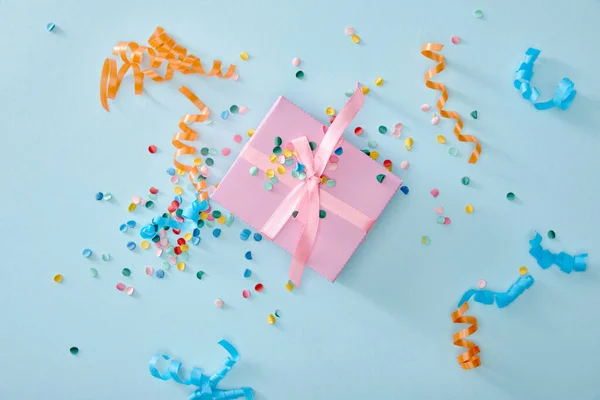 Top view of colorful confetti near pink gift box on blue background — Stock Photo