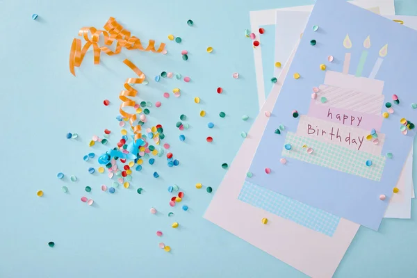 Vista superior de confeti colorido cerca de tarjetas de felicitación de cumpleaños sobre fondo azul - foto de stock