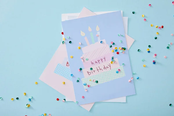 Vista superior de confetes coloridos perto de cartões de aniversário no fundo azul — Fotografia de Stock
