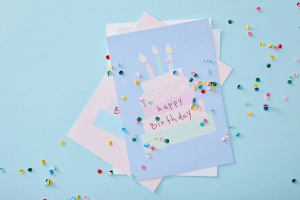 Vista superior de confeti colorido cerca de tarjetas de felicitación de cumpleaños sobre fondo azul - foto de stock