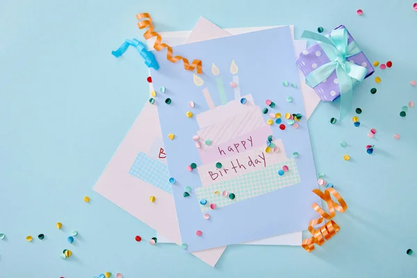 Vista superior de confeti colorido cerca de tarjetas de felicitación de cumpleaños sobre fondo azul - foto de stock