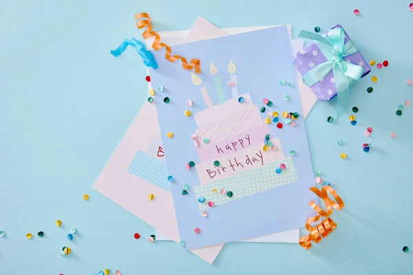 Vue du haut des confettis colorés près des cartes de vœux d'anniversaire sur fond bleu — Photo de stock