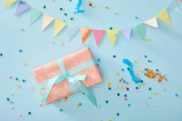 Вид сверху на красочные конфетти возле подарочной коробки на синем фоне — стоковое фото