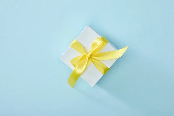 Top view of festive gift box with yellow ribbon on blue background — Stock Photo