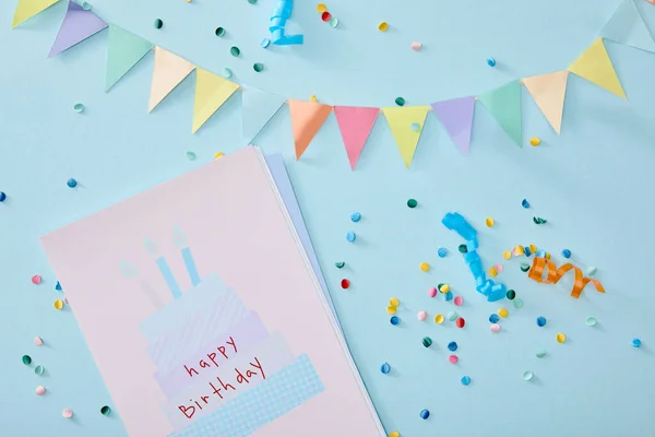 Vue du haut des confettis colorés près de la carte de vœux d'anniversaire sur fond bleu — Photo de stock