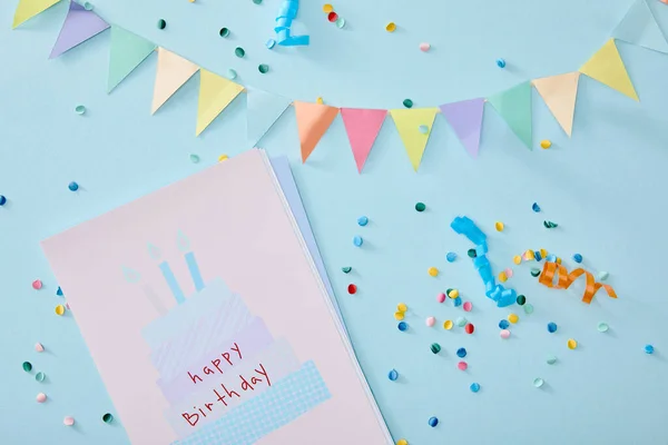 Vista superior de confeti colorido cerca de tarjeta de felicitación de cumpleaños sobre fondo azul - foto de stock