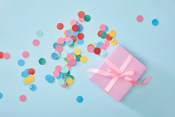 Top view of colorful confetti near pink present on blue background — Stock Photo