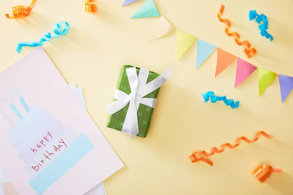 Top view of festive colorful confetti and gift with happy birthday greeting card on beige background — Stock Photo