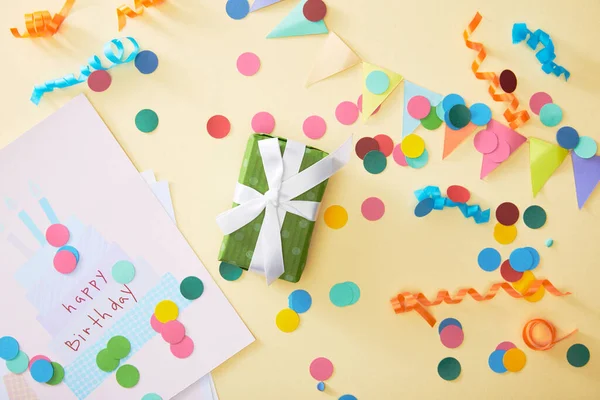 Top view of festive colorful confetti and gift with happy birthday greeting card on beige background — Stock Photo