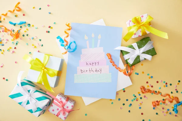 Vista superior de confeti colorido festivo, regalos y feliz cumpleaños tarjeta de felicitación sobre fondo beige - foto de stock
