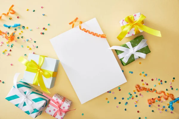 Blick von oben auf festliches buntes Konfetti und Geschenke in der Nähe von leerem Papier auf beigem Hintergrund — Stockfoto