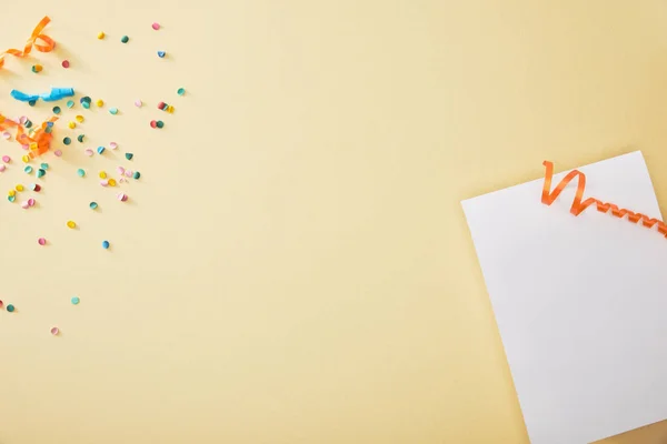 Vue du haut des confettis colorés festifs près du papier blanc sur fond beige — Photo de stock