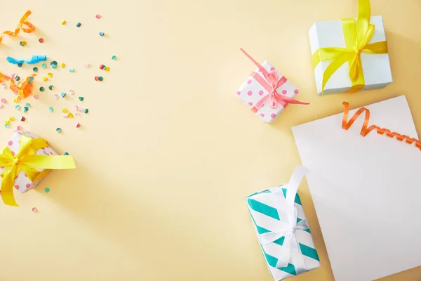 Top view of festive colorful confetti and presents near blank paper on beige background — Stock Photo