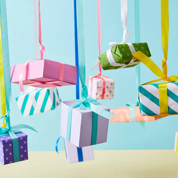 Caixas de presente coloridas festivas penduradas em fitas no fundo azul — Fotografia de Stock