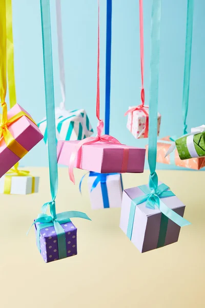 Festive colorful gift boxes hanging on ribbons on blue and yellow background — Stock Photo