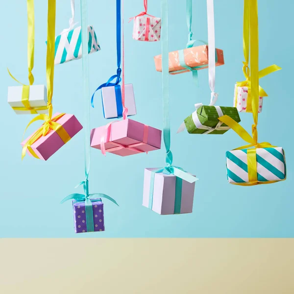 Festive colorful gift boxes hanging on ribbons on blue background — Stock Photo