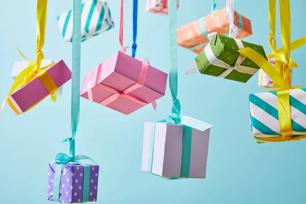 Festive colorful gift boxes hanging on ribbons isolated on blue — Stock Photo