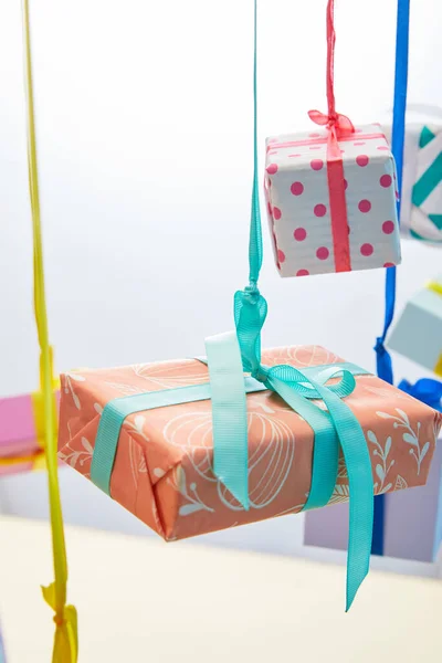 Foyer sélectif de boîtes-cadeaux colorées festives suspendues sur des rubans sur fond gris et jaune — Photo de stock