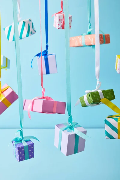 Scatole regalo colorate festive appese su nastri su sfondo blu — Foto stock