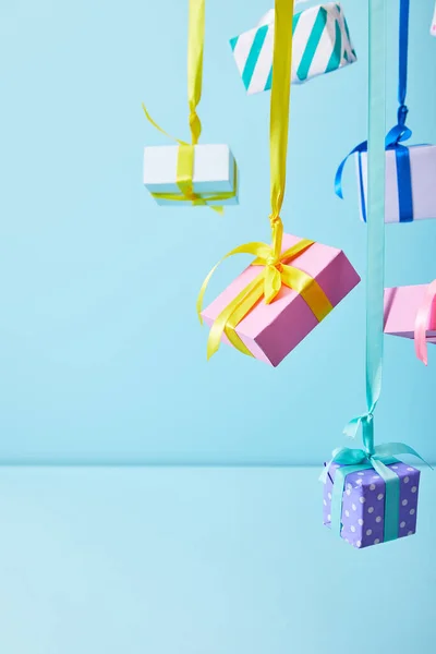 Festive colorful gift boxes hanging on ribbons on blue background — Stock Photo