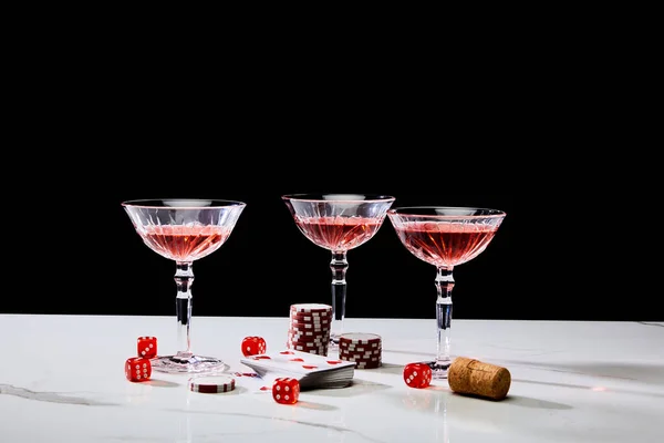 Deck of cards, glasses of cocktail, dice, casino tokens and cork on white surface isolated on black — Stock Photo