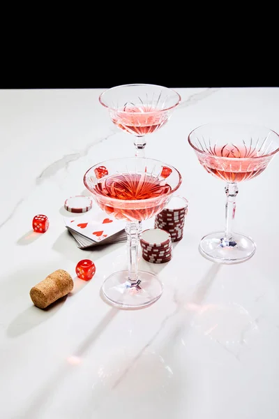 High angle view of deck of cards, glasses of cocktail, dice, casino tokens and cork on white surface isolated on black — Stock Photo