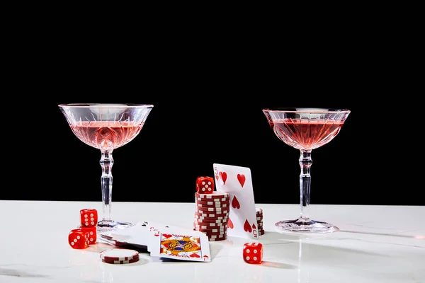 Cartes à jouer, verres de cocktail, dés et jetons de casino sur une surface blanche isolée sur noir — Photo de stock