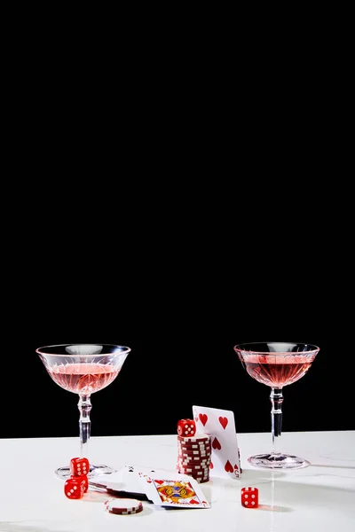 Playing cards, glasses of cocktail, dice and casino chips on white surface isolated on black — Stock Photo