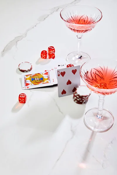Високий кут зору гральних карт, кісток і фішок казино біля келихів коктейлю на білому тлі — стокове фото