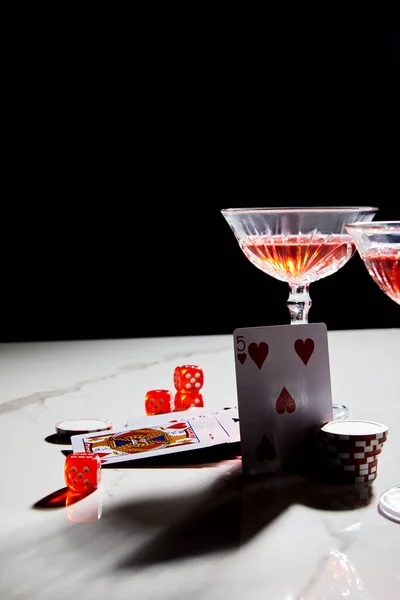Jouer aux cartes, dés et jetons de casino près de verres de cocktail sur surface blanche isolé sur noir — Photo de stock