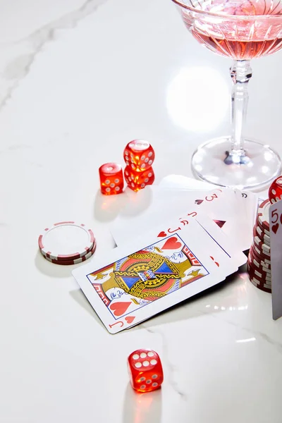 Vista de alto ángulo de jugar a las cartas, dados y fichas de casino cerca de un vaso de cóctel sobre fondo blanco - foto de stock