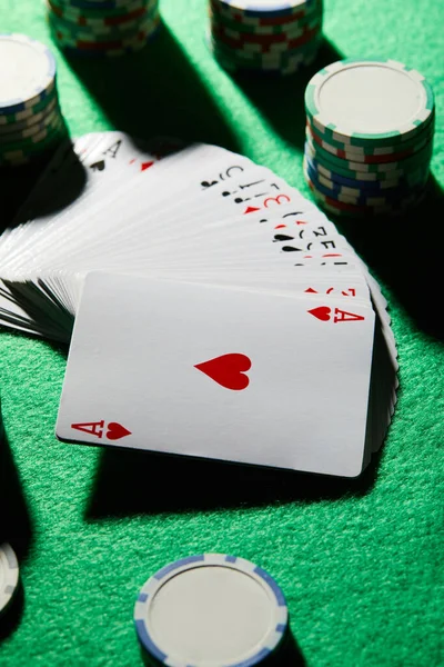 Vista de ángulo alto del paquete de tarjetas con fichas de casino en fondo verde - foto de stock