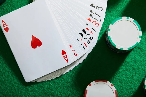 Top view of pack of cards with casino chips on green background — Stock Photo