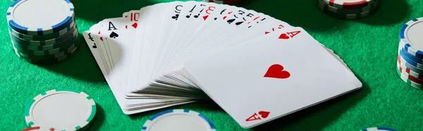 High angle view of pack of cards with casino chips on green background, panoramic shot — Stock Photo