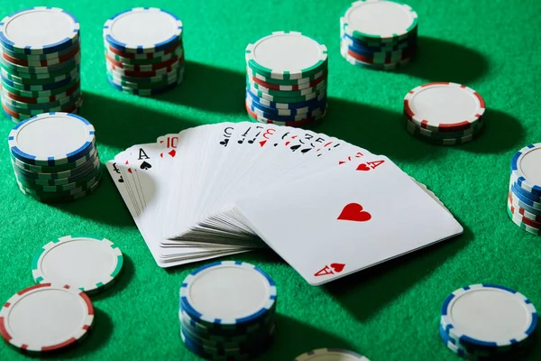 High angle view of pack of cards with casino chips on green — Stock Photo