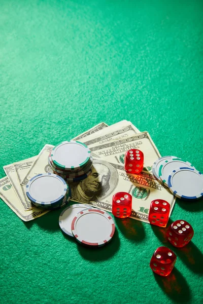 Vista de ángulo alto de billetes de dólar, dados y fichas de casino en fondo verde - foto de stock
