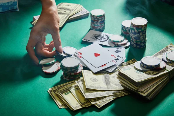 Vista parcial de la mano femenina con fichas de casino, naipes y dinero sobre fondo verde - foto de stock