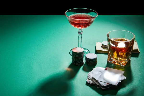 Высокий угол зрения на очки коньяк и коктейль с деньгами, фишки казино и игральные карты на зеленой поверхности изолированы на черной — стоковое фото