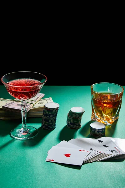 Glasses of cognac and cocktail with money, casino chips and playing cards on green surface isolated on black — Stock Photo