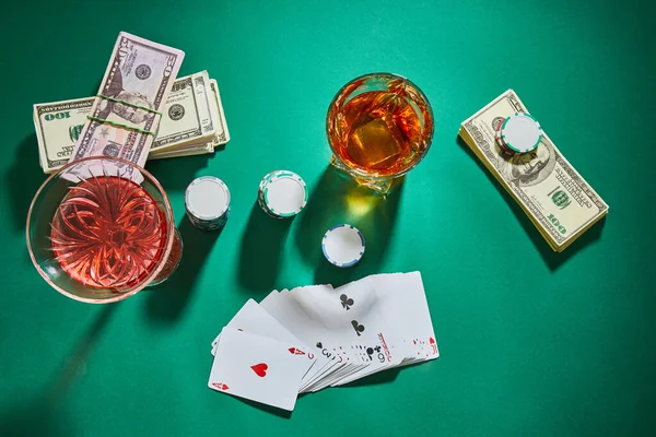 Top view of glasses of congnac and cocktail with money, playing cards and casino chips on green — стоковое фото