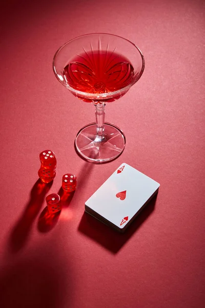 Hochwinkel-Ansicht des Cocktailglases in der Nähe des Kartendecks und der Würfel auf rotem Hintergrund — Stockfoto
