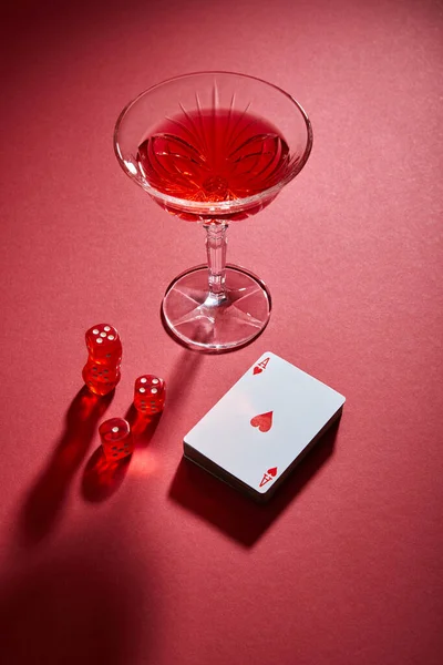 Vista de alto ángulo del vaso de cóctel cerca de la baraja de cartas y dados sobre fondo rojo - foto de stock