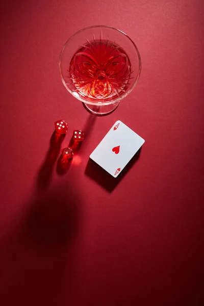 Vue du dessus du verre de cocktail près du jeu de cartes et dés sur fond rouge — Photo de stock