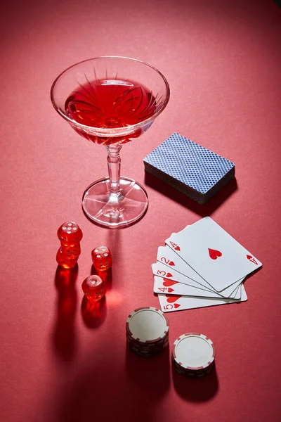 High angle view of glass of cocktail near playing cards, casino chips and dice on red background — Stock Photo